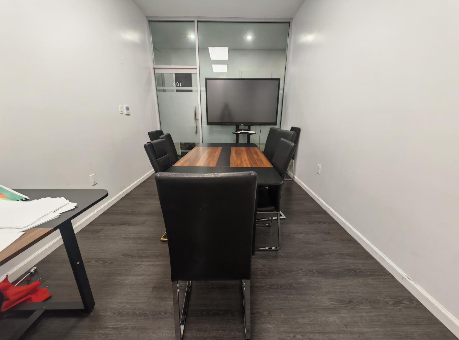 ToIvy Room 501 small meeting room with wood conference table, leather seating, and a wall-mounted smart display behind a frosted-glass door