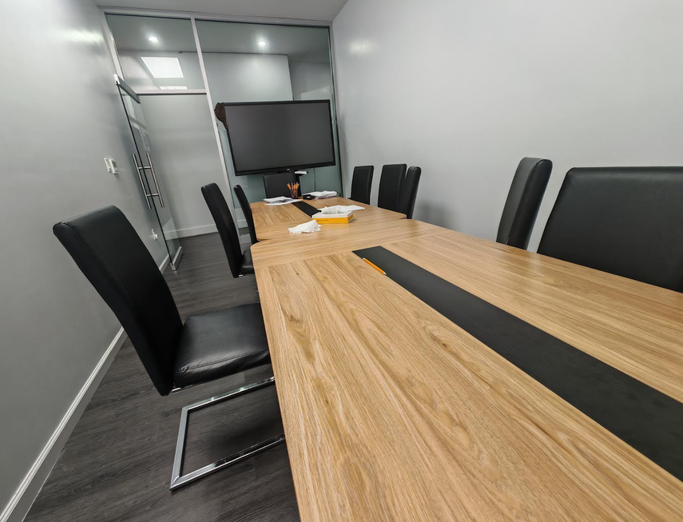 ToIvy wood-top conference room with cable channel down the table center, premium high-back leather chairs, and large smart display