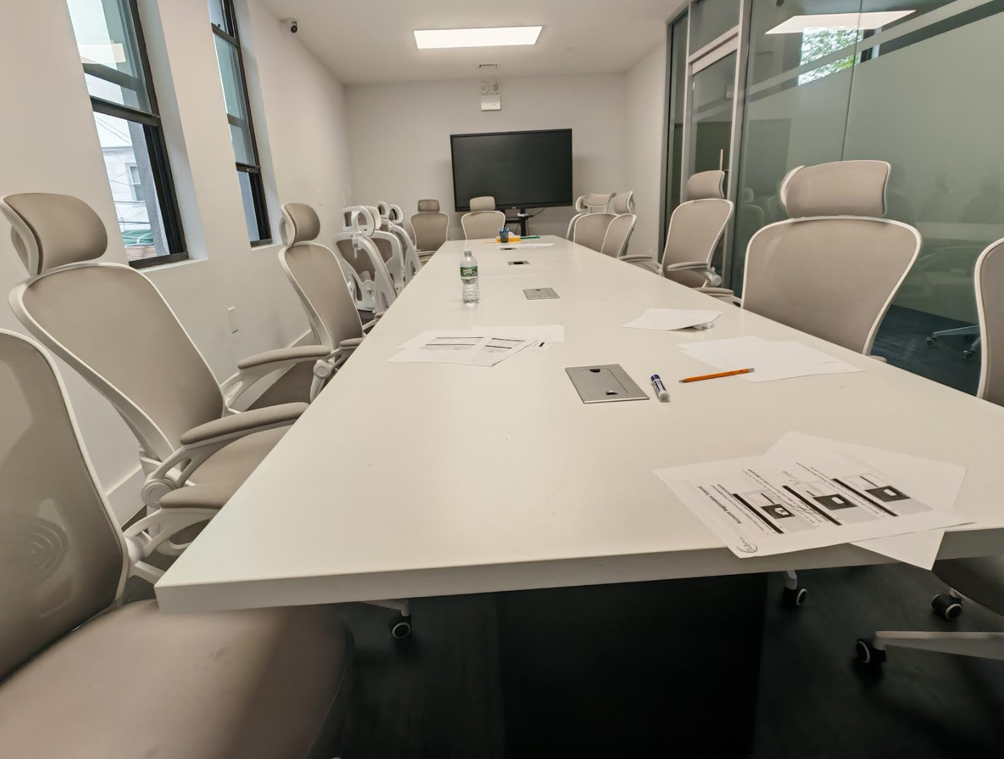 ToIvy large mock test room with a long white table set with practice exams, mesh ergonomic chairs, and a wall-mounted smart display