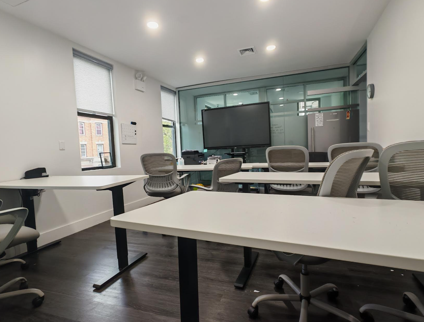 ToIvy open study area with adjustable-height desks, ergonomic chairs, and a glass-walled smart-display classroom in the background